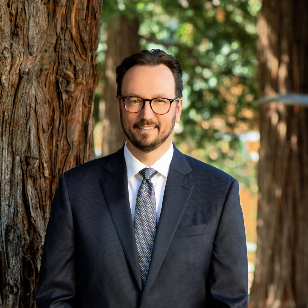 Person wearing glasses and a suit with trees in the background.