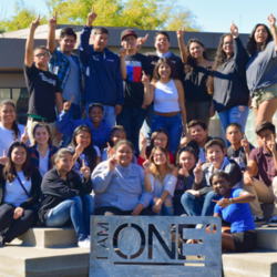Students standing behind a sign that reads I am one