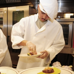 Chef putting food on a plate in a kitchen